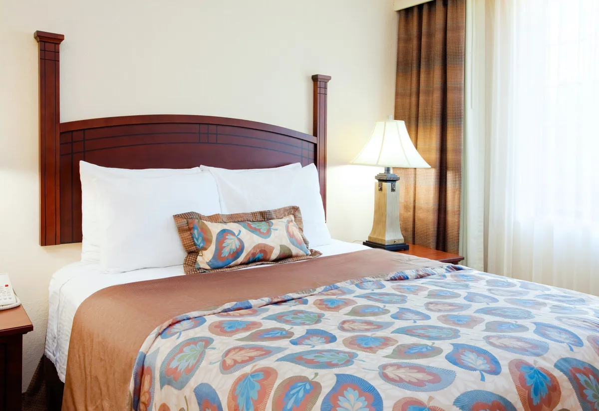 This image features a cozy bedroom setting with a plush bed, decorative pillows, and a soft lampshade beside the bed. The mood is calm and relaxing, emphasizing rest and comfort—ideal for unwinding after a busy day.