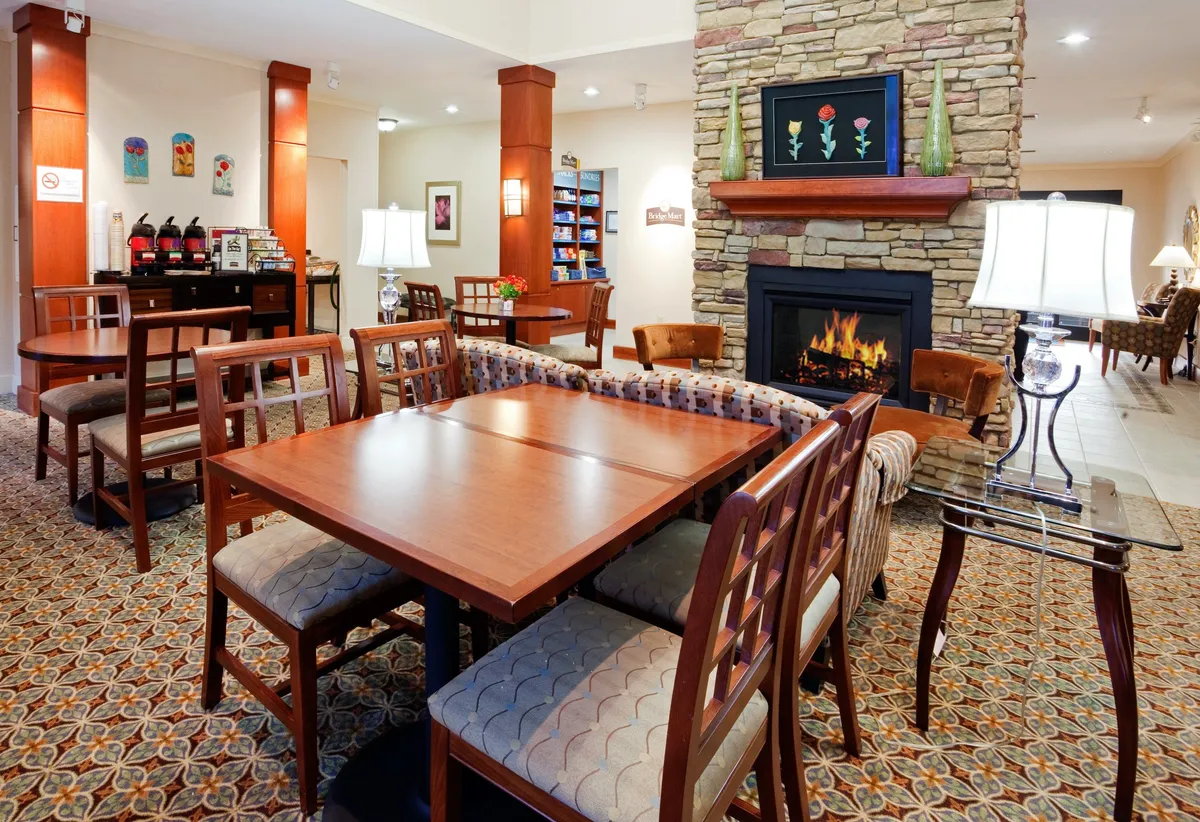 A warm, inviting room with a stone fireplace, wooden furniture, decorative artwork, and soft lighting from lamps. The setting exudes a spa-like ambiance, ideal for quiet moments and self-care, reminiscent of a spa-inspired bathroom.